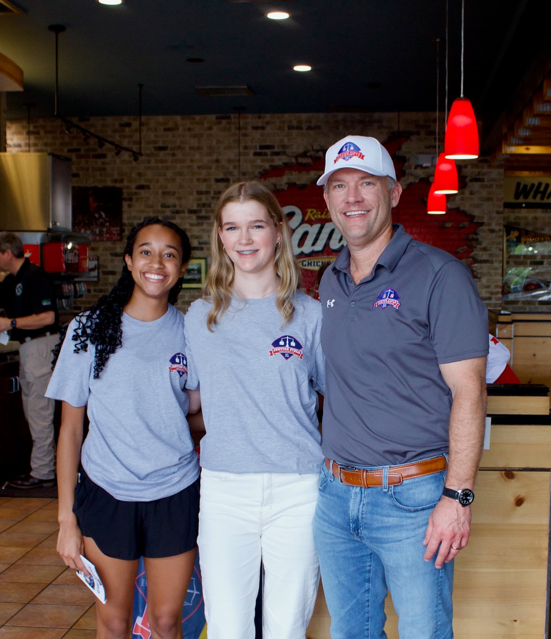 Scott Chafin posing with two girls at the Justice Field Day event at Raising Canes