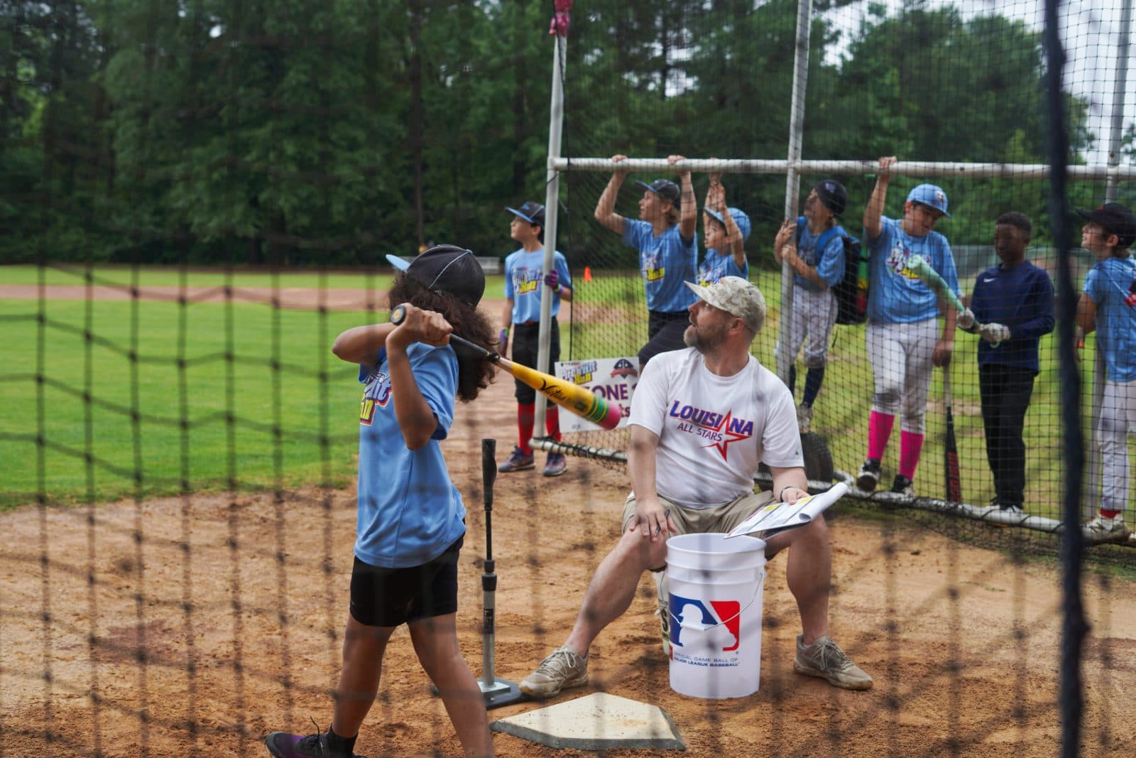 A player hitting off the tee in the cage while a coach watches.