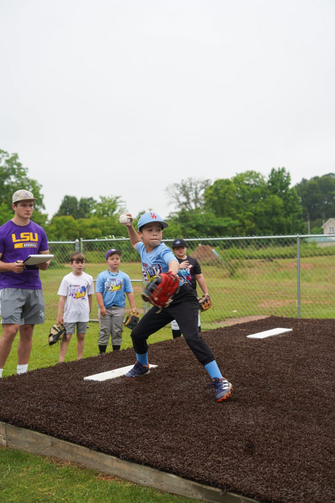 A young player pitching off the mound as others watch.