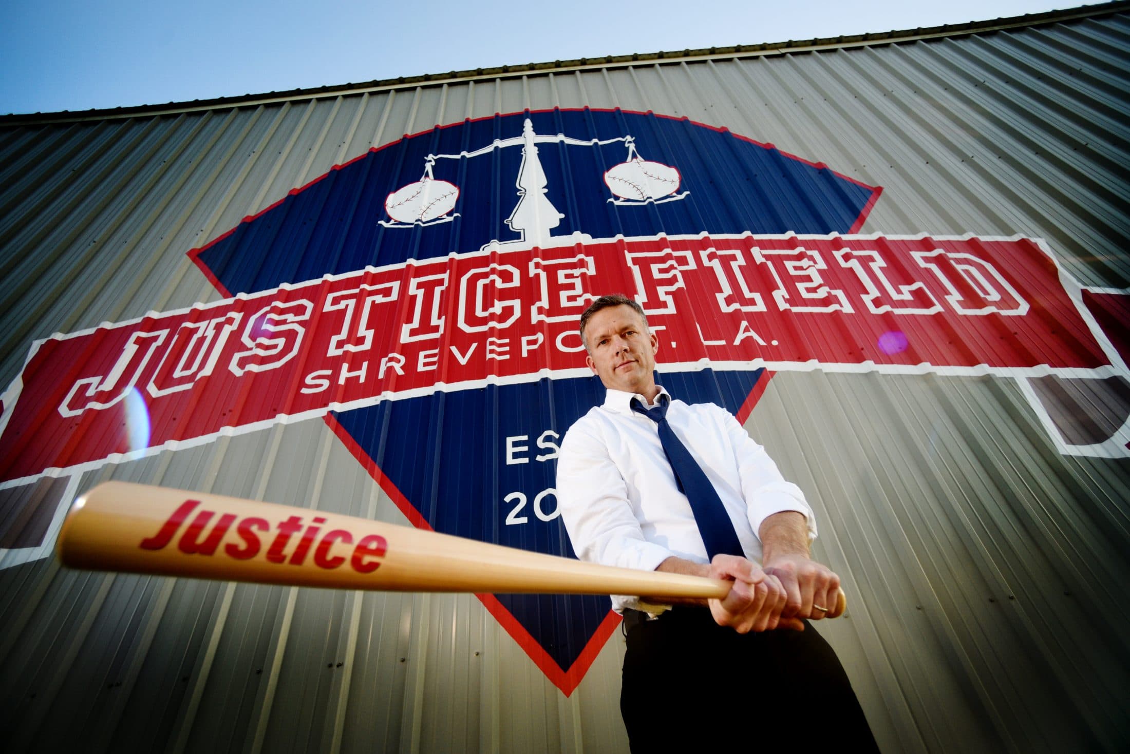 Scott Chafin holding a Justice bat in front of the painted Justice Field mural logo.