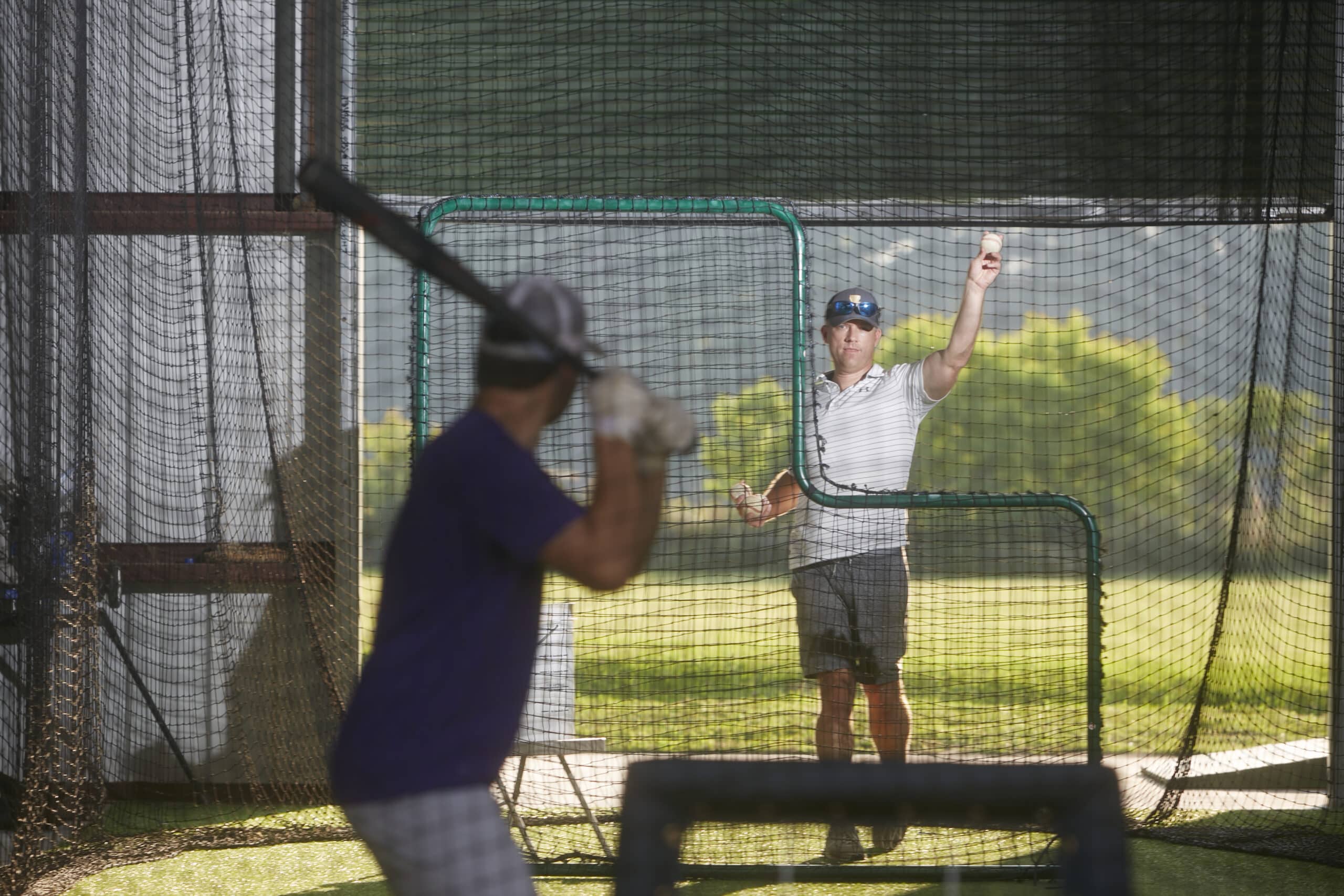 Scott pitching to a batter in the batting cage at Justice Field.