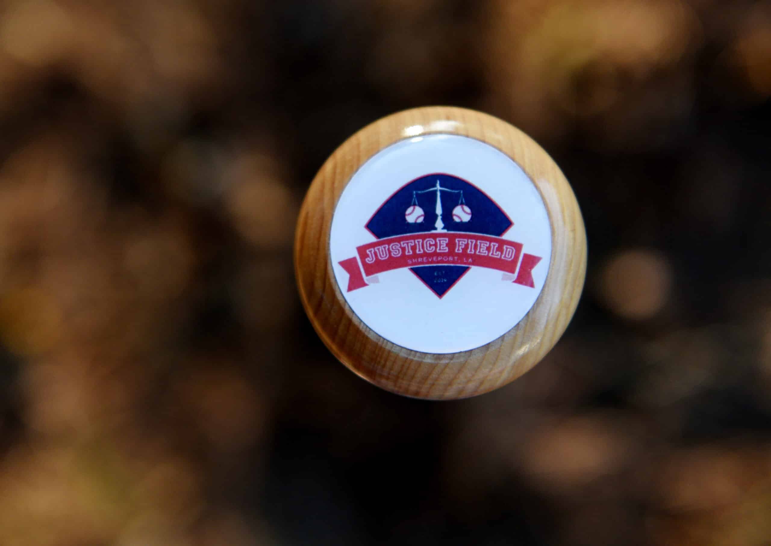 The Justice Field logo medallion on the knob of a wooden bat.